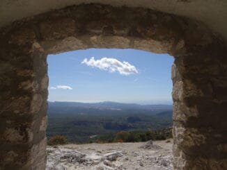 Vue panoramique d'une vallée verdoyante sous un ciel bleu, encadrée par la fenêtre d'une ruine ancienne, métaphore de la recherche de la lumière et de l'espoir.