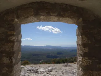 Vue panoramique d'une vallée verdoyante sous un ciel bleu, encadrée par la fenêtre d'une ruine ancienne, métaphore de la recherche de la lumière et de l'espoir.