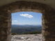 Vue panoramique d'une vallée verdoyante sous un ciel bleu, encadrée par la fenêtre d'une ruine ancienne, métaphore de la recherche de la lumière et de l'espoir.