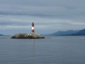 Phare symbolisant la recherche de la vérité, situé sur un îlot rocheux, avec un paysage marin et montagneux en arrière-plan sous un ciel partiellement nuageux.
