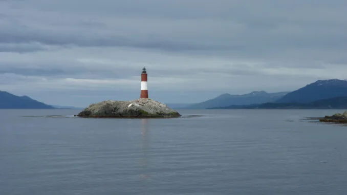 Phare de Vérité Phare symbolisant la recherche de la vérité, situé sur un îlot rocheux, avec un paysage marin et montagneux en arrière-plan sous un ciel partiellement nuageux.