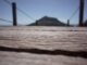 Un pont en bois en premier plan avec une mise au point rapprochée sur sa texture, menant au flou d'une montagne éloignée sous un ciel bleu, métaphore d'un voyage vers la sagesse.