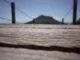 Un pont en bois en premier plan avec une mise au point rapprochée sur sa texture, menant au flou d'une montagne éloignée sous un ciel bleu, métaphore d'un voyage vers la sagesse.