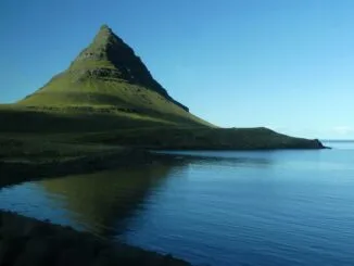 Montagne isolée se reflétant dans un lac paisible sous un ciel bleu.