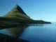 Montagne isolée se reflétant dans un lac paisible sous un ciel bleu.