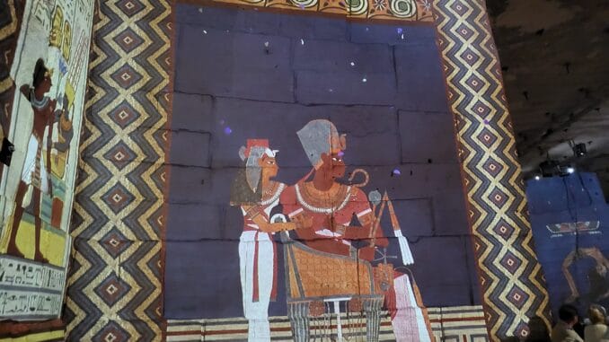 Fresque égyptienne projetée, figures royales et motifs géométriques dans une exposition immersive.